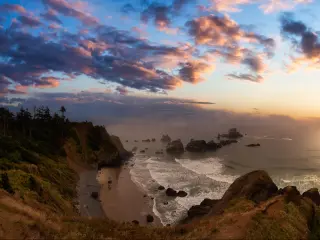 Panoramic view of sandy and rocky beach with waves breaking in crescent bay and dramatic sunset sky