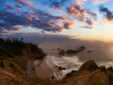Panoramic view of sandy and rocky beach with waves breaking in crescent bay and dramatic sunset sky