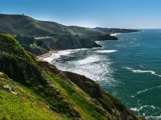 Half Moon Bay, California with hills to the side and the ocean on the right with a sandy bay and blue sky.