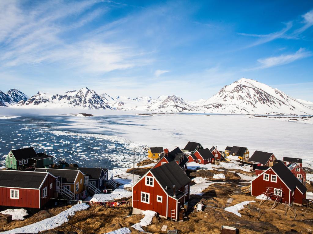 Typical Greenland village on the coast with ice-covered mountains in the background.