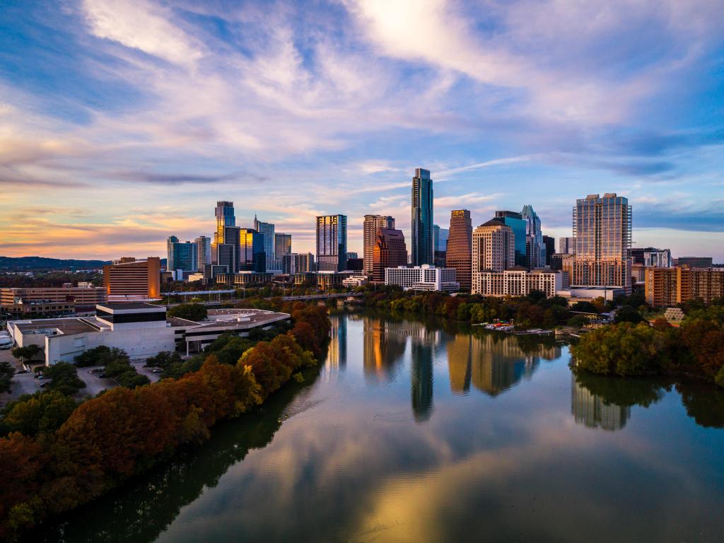 High rise buildings reflected into still lake with autumn leaves on trees around the lake and a blue sky with clouds