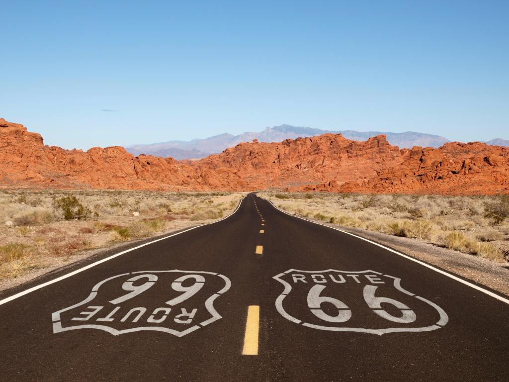 Route 66 pavement sign with Mojave desert red rock mountains.