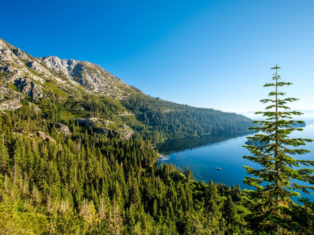 Lake Tahoe, California, USA landscape with trees lining the stunning lake, mountains and against a clear blue sky.