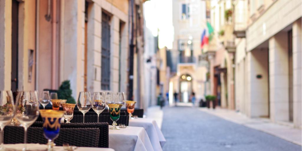 Wine glasses sitting on tables outside a restaurant on a cobbled street in Bologna, Italy