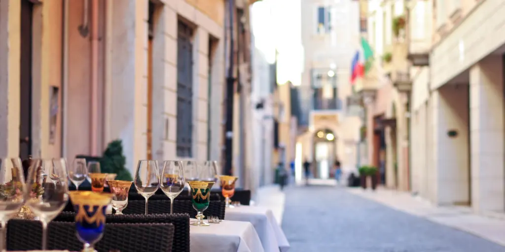 Wine glasses sitting on tables outside a restaurant on a cobbled street in Bologna, Italy