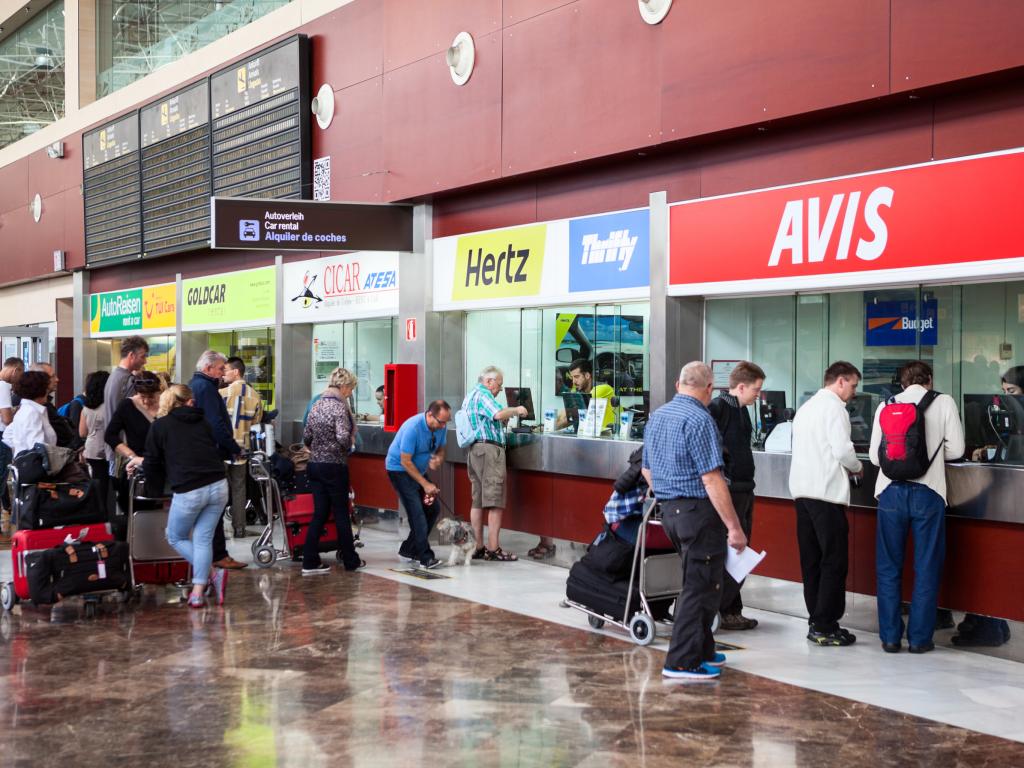 Stands of major car rental companies are at airport with customers in a queue