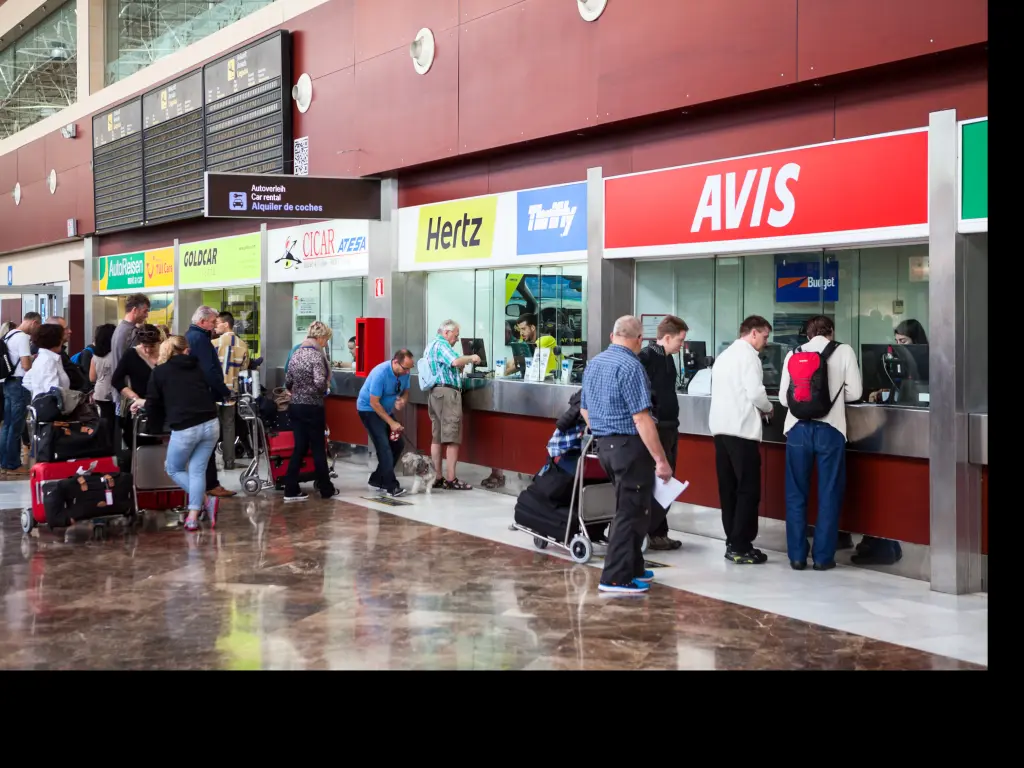 Stands of major car rental companies are at airport with customers in a queue