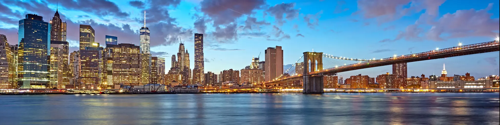 New York City, USA with the Manhattan skyline and Brooklyn Bridge as seen from across the East River at dusk. 