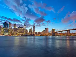 New York City, USA with the Manhattan skyline and Brooklyn Bridge as seen from across the East River at dusk. 