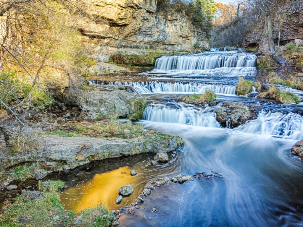 Willow River Falls, USA taken on a late afternoon day during fall with small waterfalls leading down to the water in the fore ground and rocky terrain in the distance. 