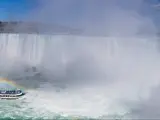 A panoramic view of Niagara Falls with a boat near the mist from the water that creates a rainbow.