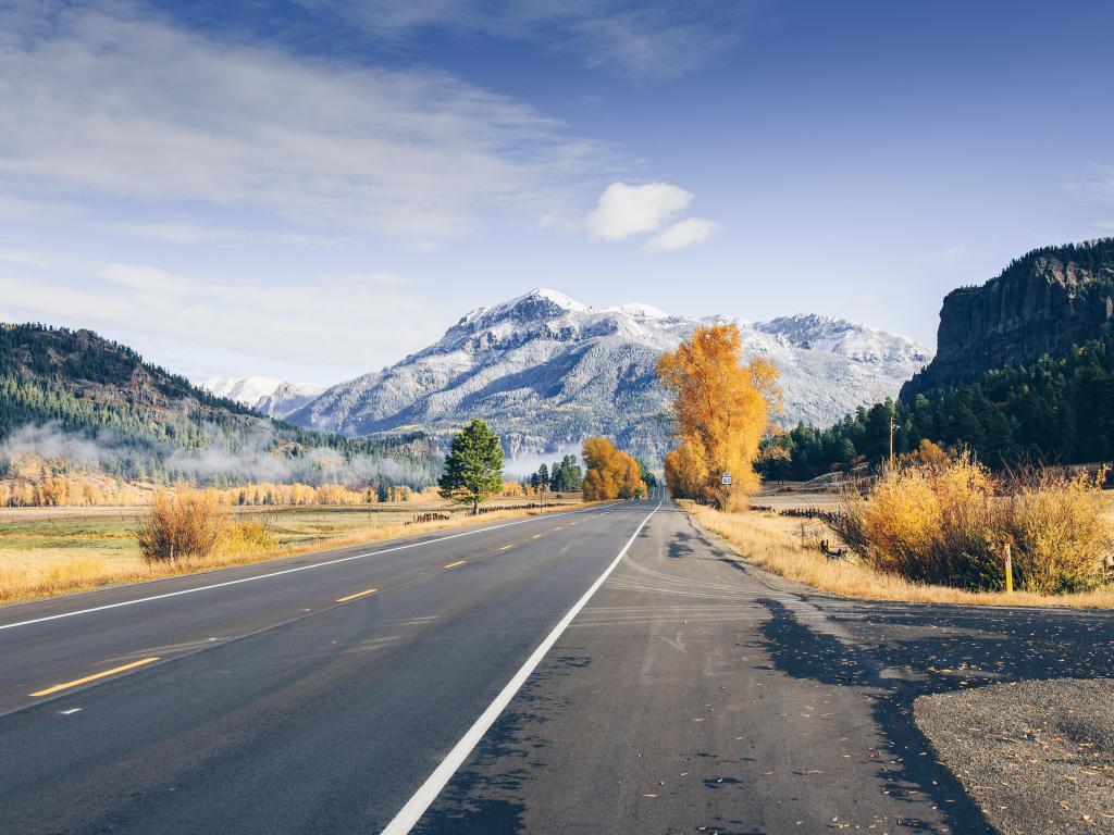 Fall colors lining up well-maintained highway with a snow-capped mountain in the background