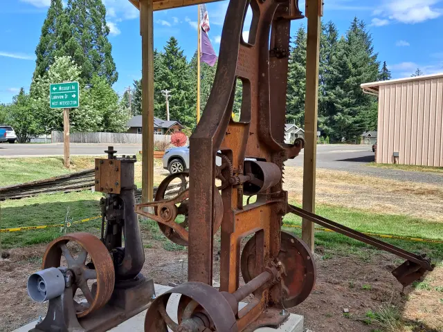 Historic logging equipment on display outside the museum with a road visible in the background