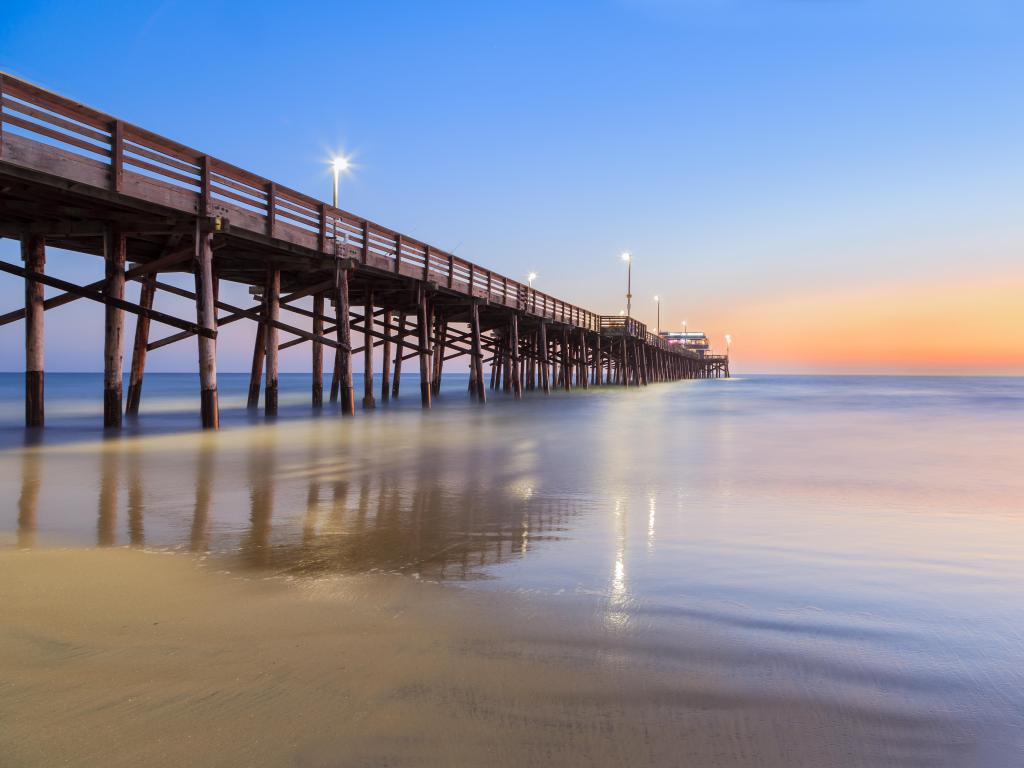 Newport Beach, California, USA with a view of Balboa Pier after sunset with calm sea surrounding it and beach in the foreground. 