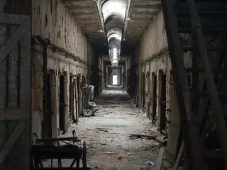 An dark and eerie derelict hallway within the abandoned Eastern State Penitentiary building, with light streaming in from a distant doorway