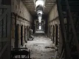 An dark and eerie derelict hallway within the abandoned Eastern State Penitentiary building, with light streaming in from a distant doorway