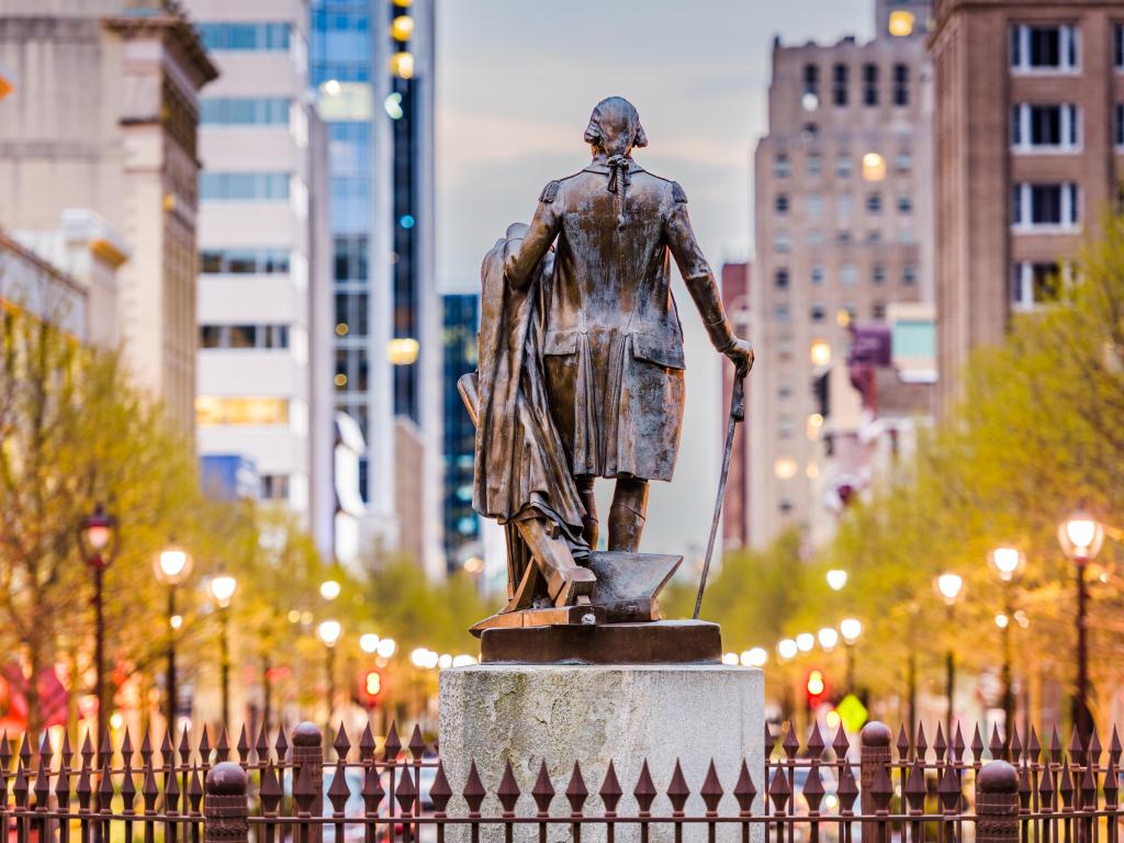 Statue outside state capitol viewed from behind, looking out toward high rise downtown buildings (slightly blurred)