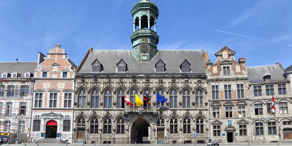 The Gothic exterior of the City Hall, Mons, Belgium, with Belgian and European flags, and a scooter parked in front