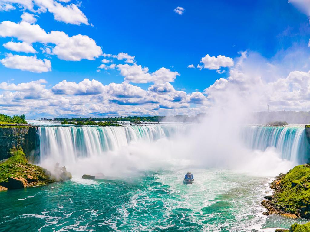 Niagara Falls, USA taken on a sunny day with a boat in the foreground and water spray lifting in the air.