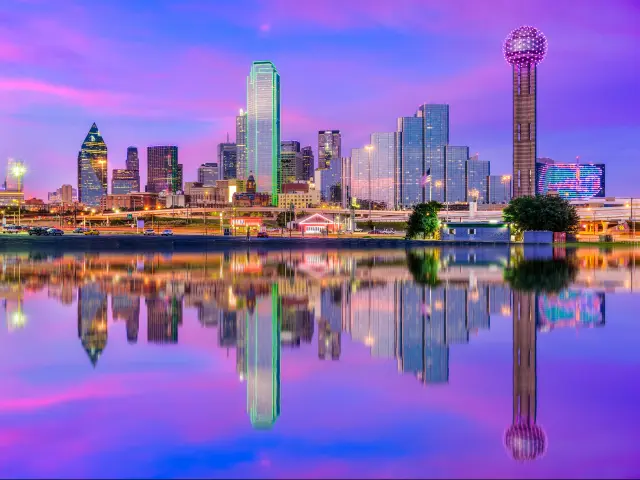 Dallas, Texas, USA downtown city skyline at night with the skyscrapers reflecting in the water in the foreground.