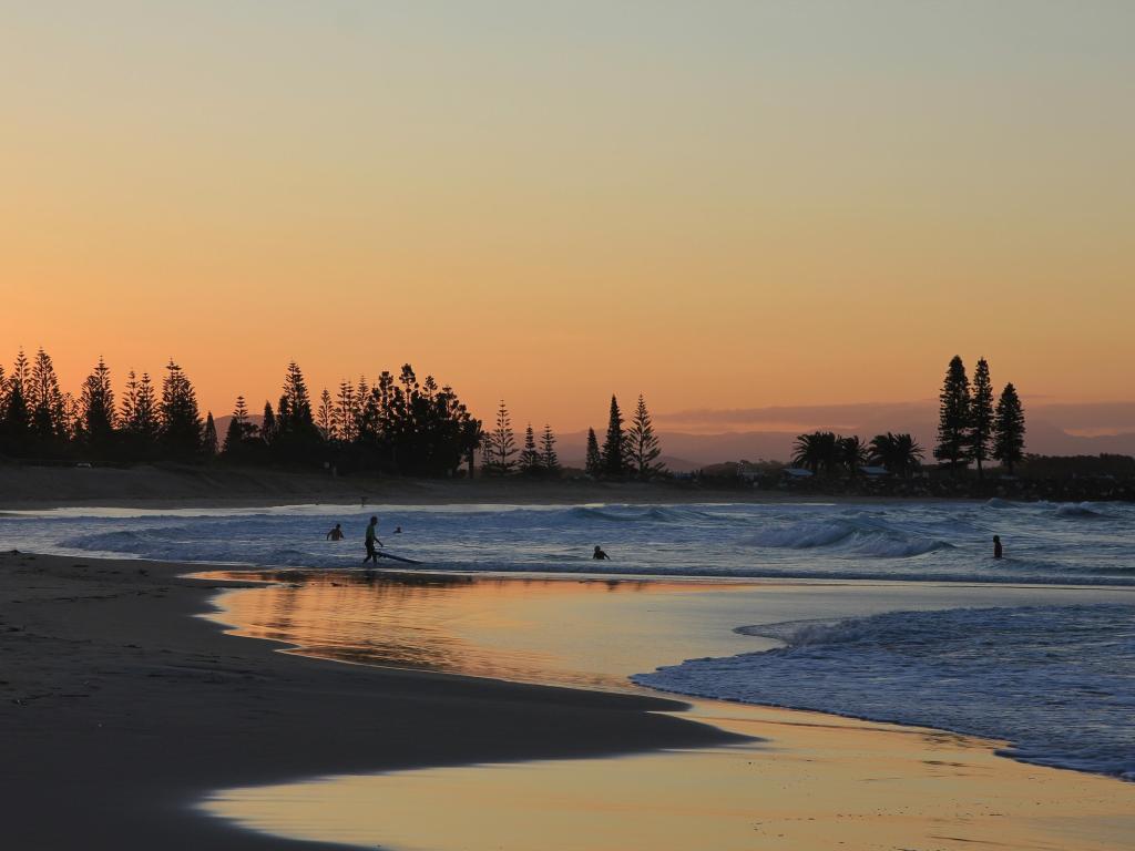 Surfers on a calm beach in low, golden sunset light