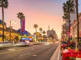 Los Angeles, California, USA with traffic and sports cars on Hollywood Boulevard at dusk with palm trees and iconic buildings in the distance.