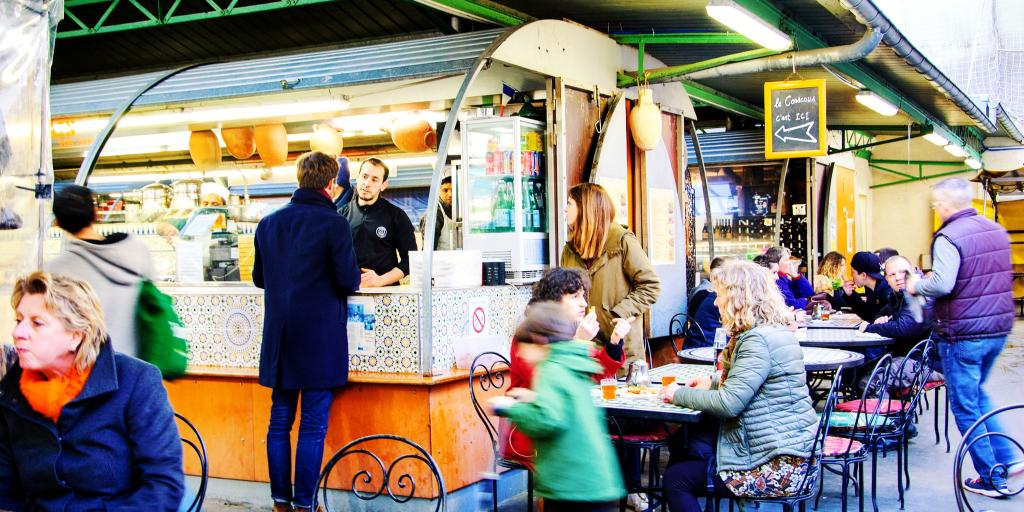 People visit the food stalls and sit at tables at Marche des Enfants Rouges, a covered market in Paris