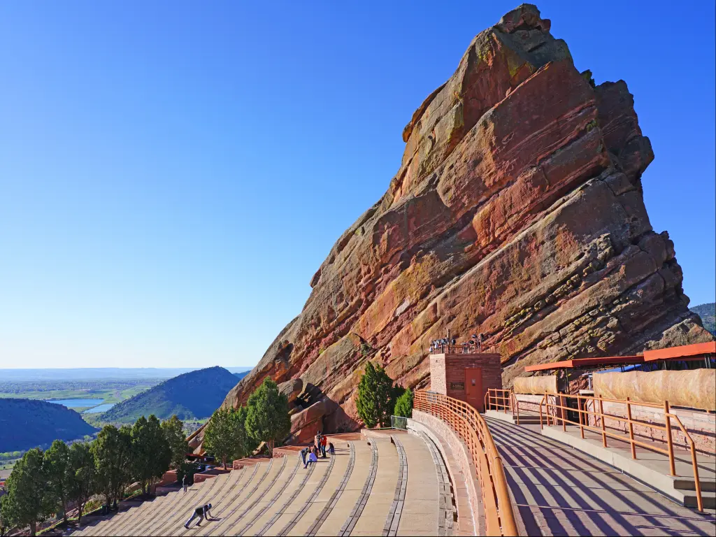 A picturesque view of the Historic open-air Red Rocks Amphitheatre with a couple of people sitting in the benches enjoying the view of the mountains from afar early in the morning in Denver