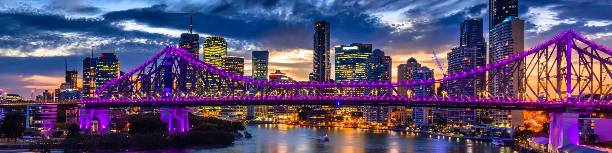 Brisbane, Australia with a vibrant night time panorama of Brisbane city with purple lights on Story Bridge.