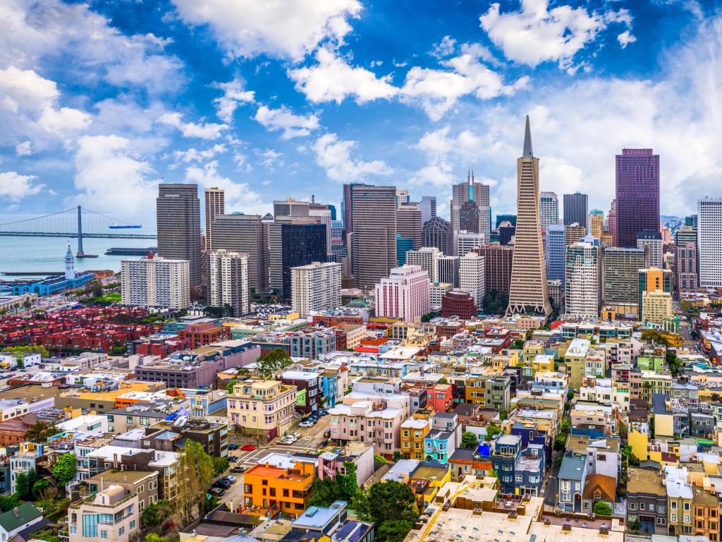 San Francisco, California, USA city skyline with a bridge in the distance, colorful buildings in the foreground against a blue sky.