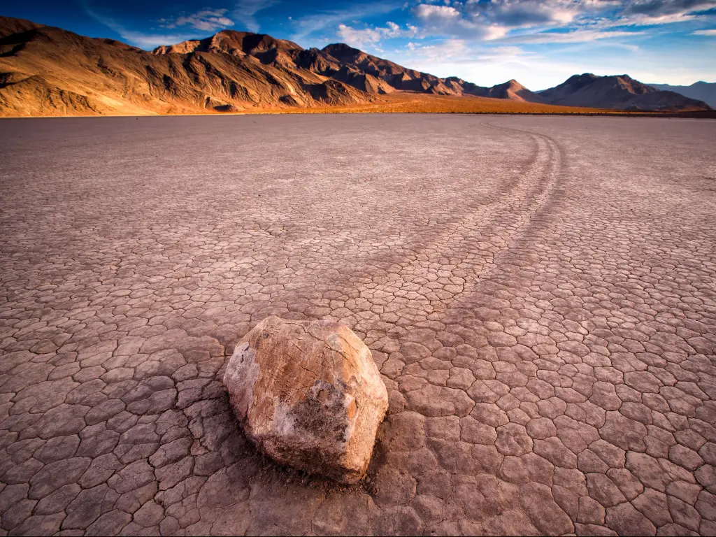 Racetrack Playa, Death Valley National Park, USA with a sunset view of The Racetrack, a dry lake feature stone in the foreground and badlands in the distance.