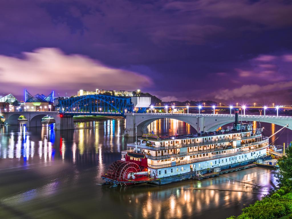 Chattanooga, Tennessee, USA downtown over the Tennessee River with a large boat in the foreground taken at night.