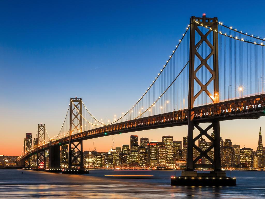 Silhouette of Bay Bridge with cityscape showing many illuminated windows in the background