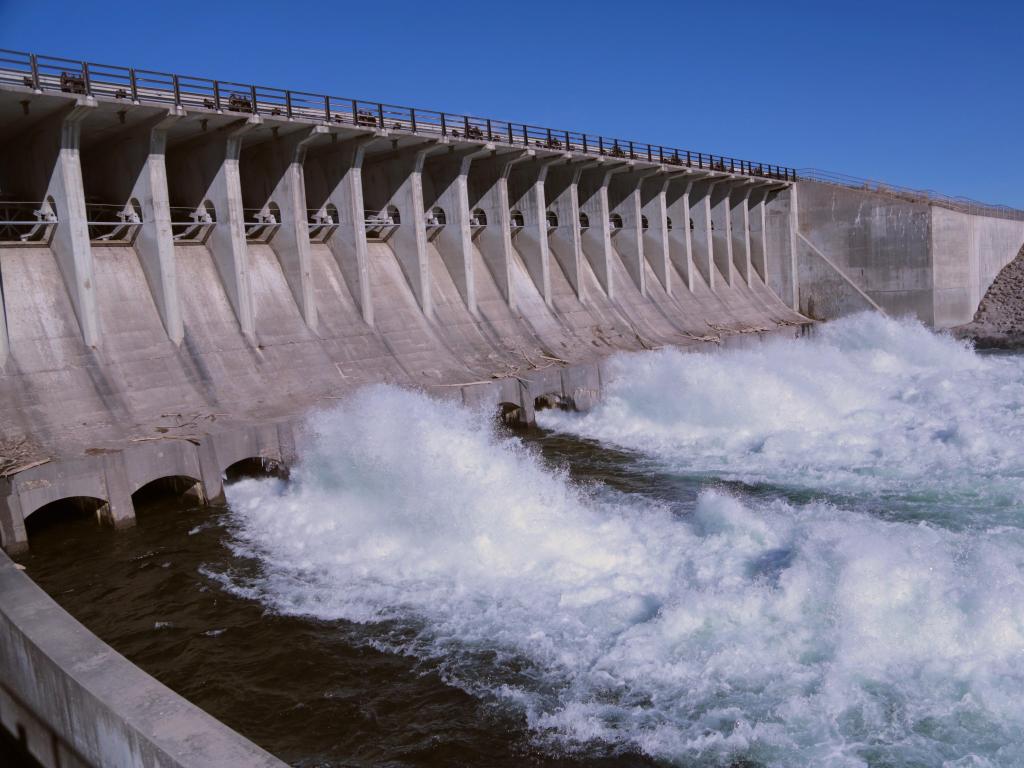 Jackson Lake dam in the Grand Teton National Park near Jackson Wyoming with rushing water and bright blue sky.