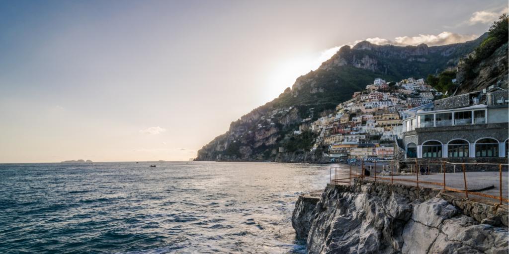 The sun sets behind a mountain at Fornillo Beach in Positano along the Amalfi Coast