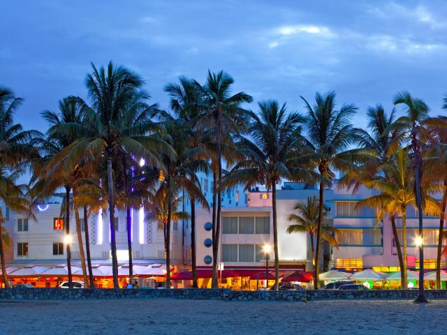 Art Deco buildings illuminated in neon colors with beach and palm trees in the foreground