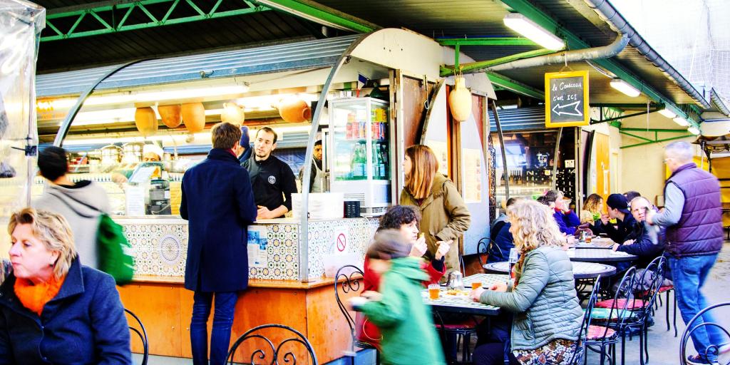 People visit the food stalls and sit at tables at Marche des Enfants Rouges, a covered market in Paris