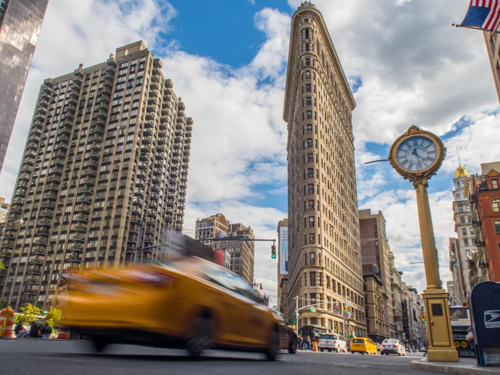 A yellow taxi driving on the road with the famous Flatiron Building in the background
