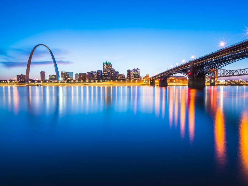 high rise buildings lit up at night with reflection in calm river, with bridges and arch monument