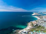 Aerial drone shot over Newport Beach in Orange County, with coastal homes, blue skies, beaches and harbor entrance in view.