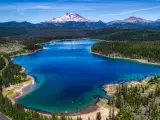 Aerial panorama of Elk Lake near Bend, Oregon, with the deep blue and turquoise lake sitting in front of snow capped mountains, under a blue sky