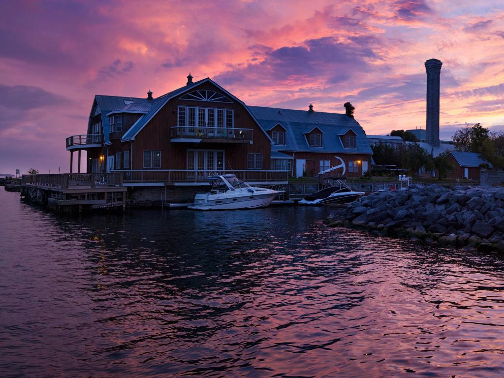 Kingston, Ontario, Canada with a stunning sunset over the harbor and calm water in the foreground. 