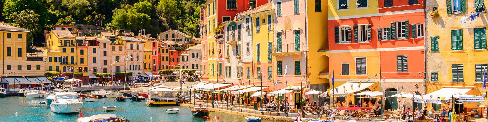 Boats in the turquoise blue water of the harbour in Portofino, Italy, with colourful townhouses in the background