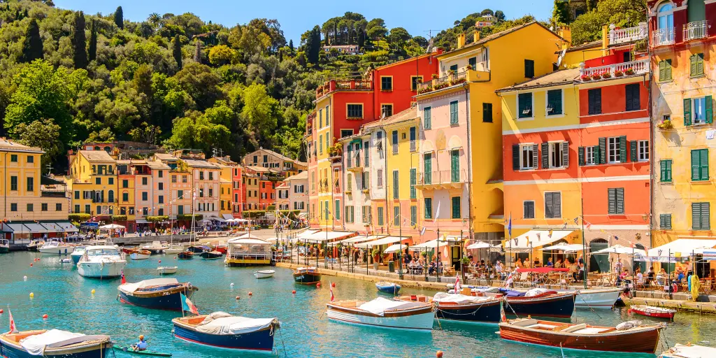 Boats in the turquoise blue water of the harbour in Portofino, Italy, with colourful townhouses in the background