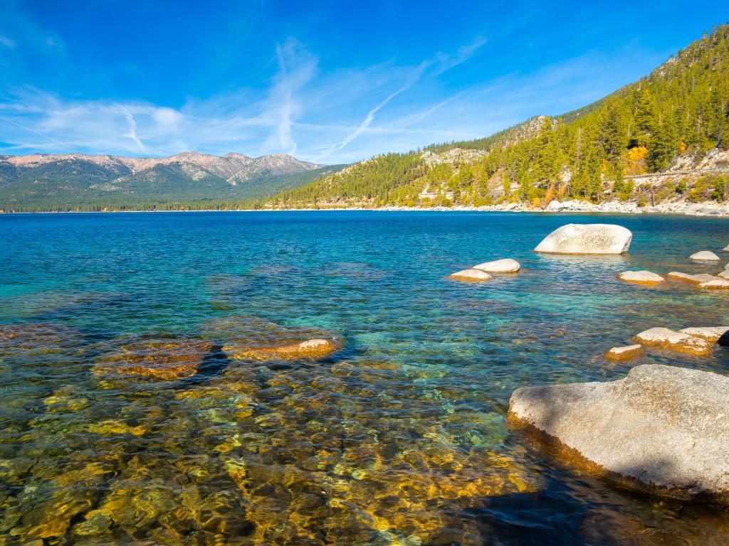 Lake Tahoe, California, USA with rocks at the lakeside on a sunny day and mountains in the distance.