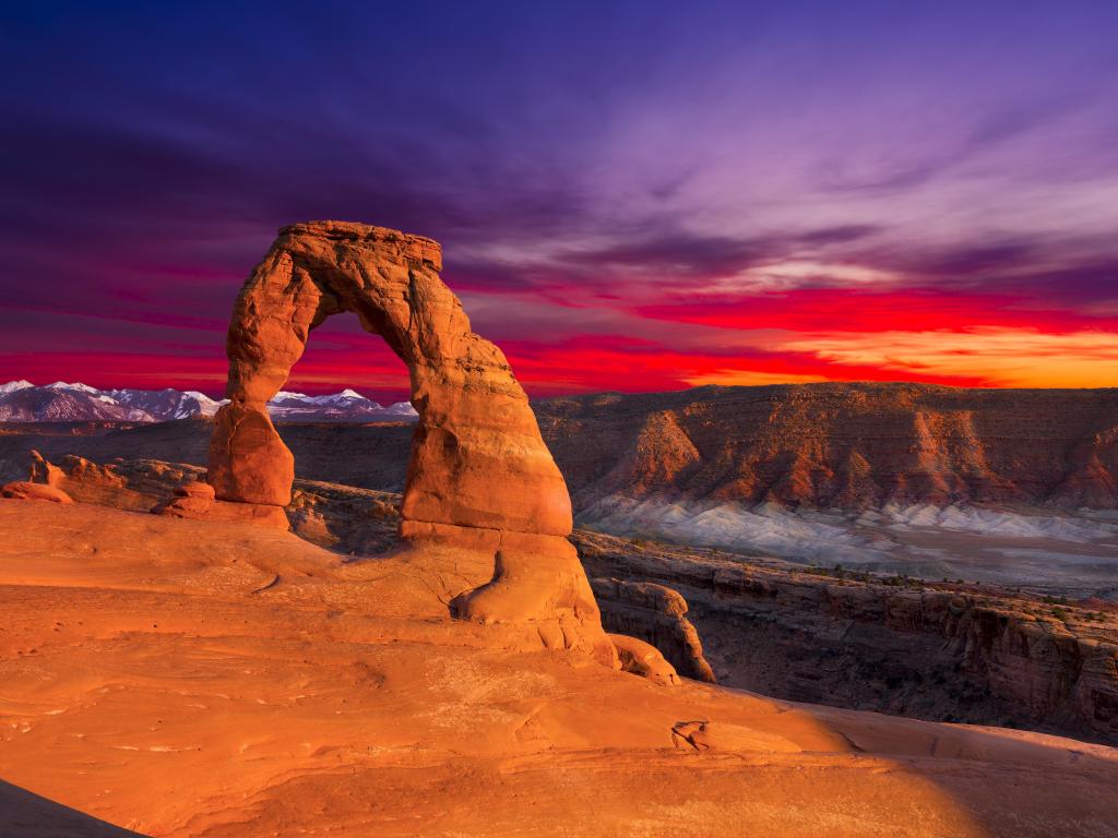 Red rock arch with wide view behind, lit up in vibrant red sunset light