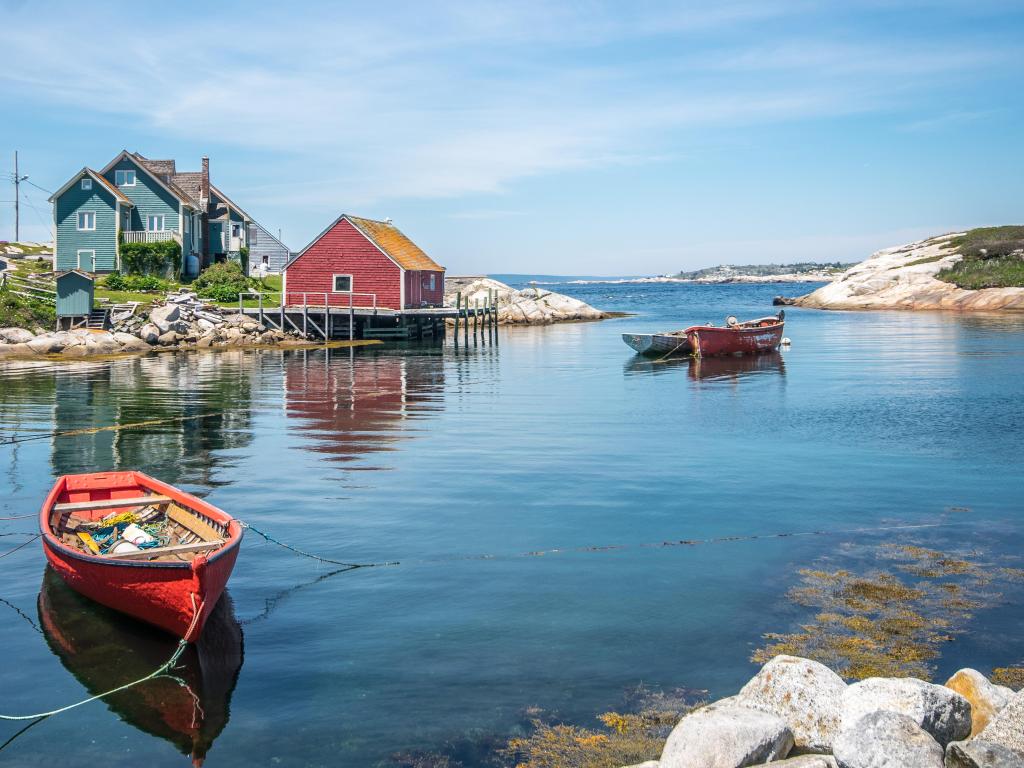 Small red and blue boats in a calm bay with red barn type building on the shore