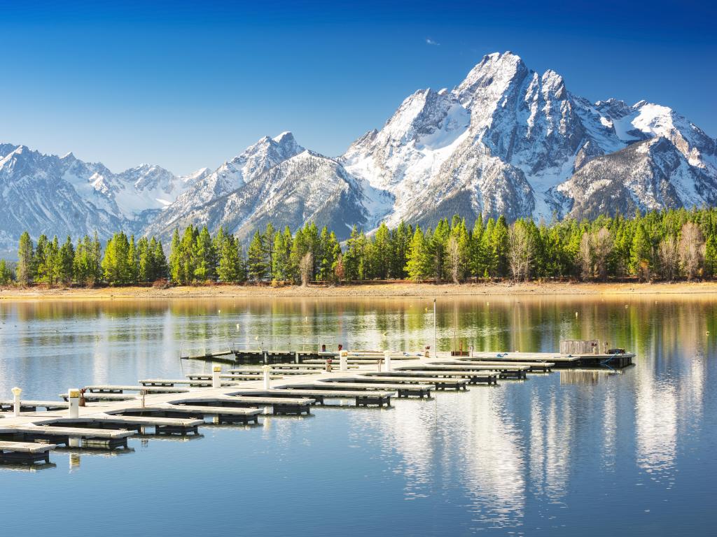 Boat docks on clear lake with blue skies, snow-capped mountain in the background