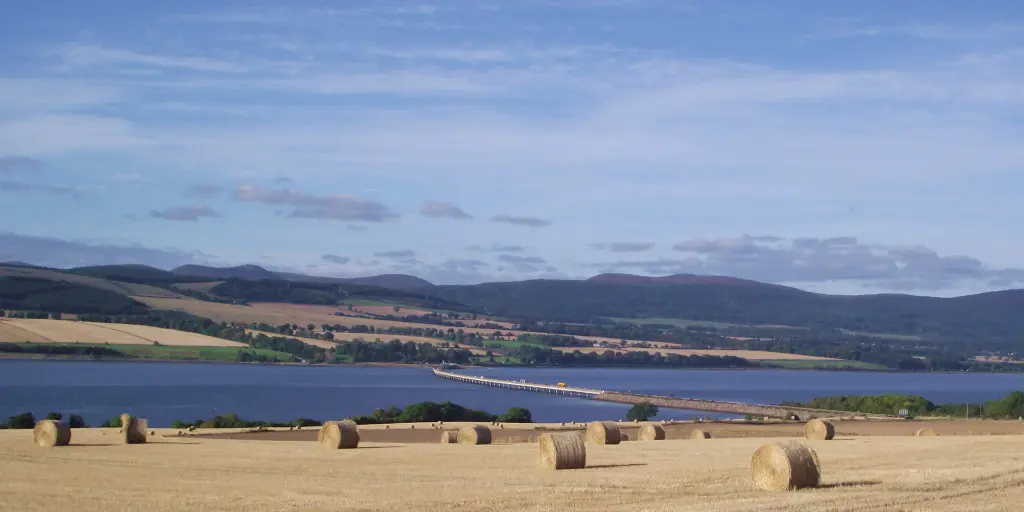 A view across hay fields and hay bails to the water in the Black Isle, Scotland.