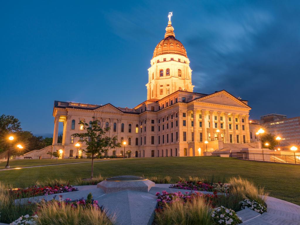 State Capitol building in Topeka, Kansas, lit up at night, with flowers in the foreground